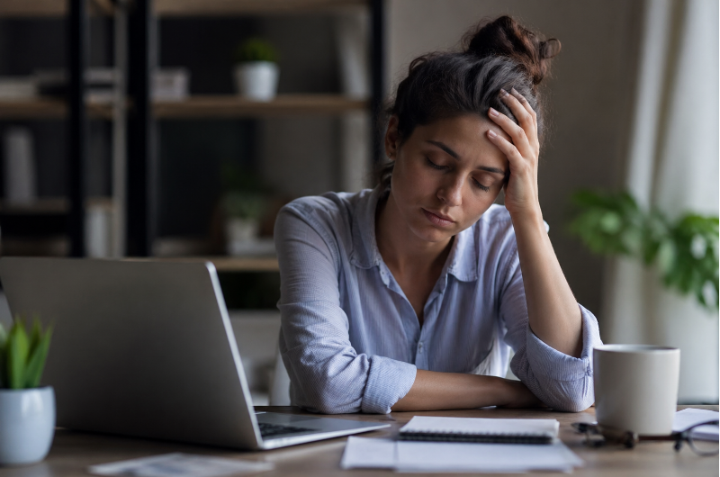 Mulher com expressão de cansaço emocional trabalhando no computador, representando viver no automático e a importância da consulta online com psiquiatra